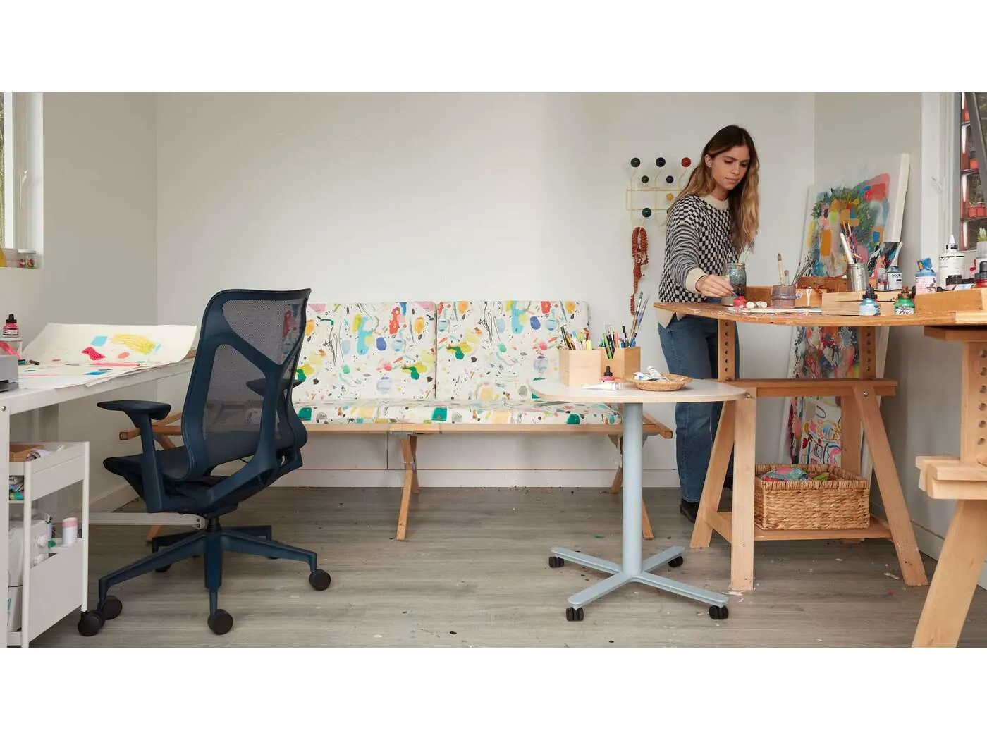 Kindah Khalidy painting at a worktable in her Berkeley studio, surrounded by her own bright abstract canvases