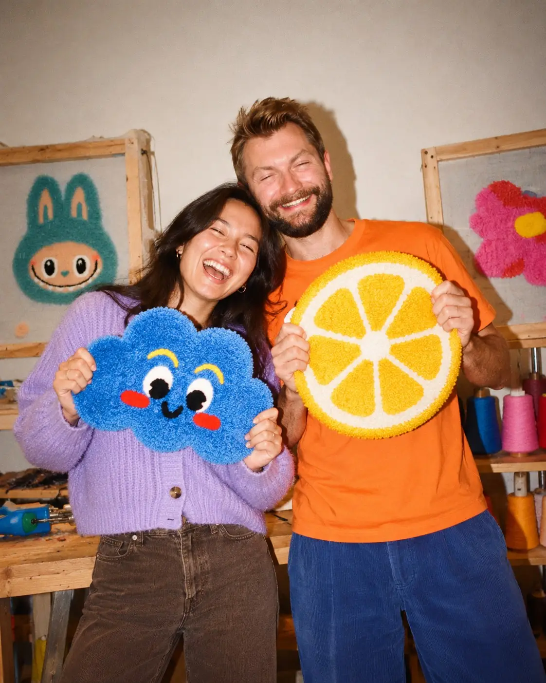 Two people holding up the tufted pieces they made together
